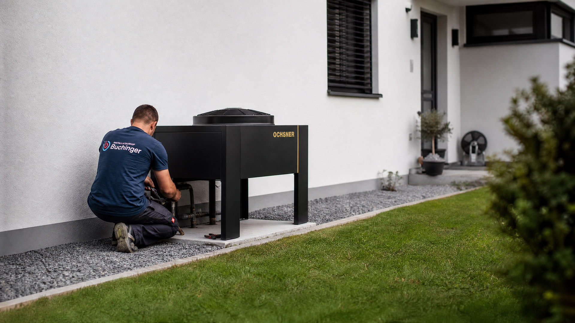Monteur installiert die Außeneinheit einer Wärmepumpe vor einem Einfamilienhaus